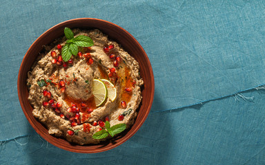 Wall Mural - homemade spread of baked eggplant baba ganoush in a bowl with pomegranate seeds, lime, olive oil and lime slices on a blue linen tablecloth