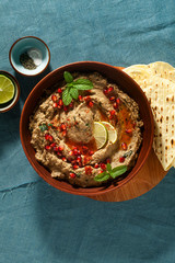 Wall Mural - homemade spread of baked eggplant baba ganoush in a bowl with pomegranate seeds, lime, olive oil and lime slices on a blue linen tablecloth with flat bread