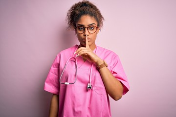 Poster - African american nurse girl wearing medical uniform and stethoscope over pink background asking to be quiet with finger on lips. Silence and secret concept.