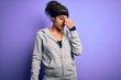 © Krakenimages.com - Young african american sportswoman doing sport wearing sportswear over purple background tired rubbing nose and eyes feeling fatigue and headache. Stress and frustration concept.