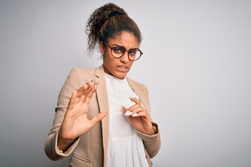 Wall Mural - Beautiful african american businesswoman wearing jacket and glasses over white background disgusted expression, displeased and fearful doing disgust face because aversion reaction. With hands raised