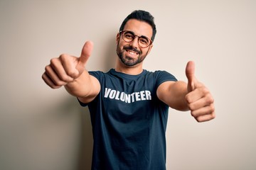 Canvas Print - Handsome man with beard wearing t-shirt with volunteer message over white background approving doing positive gesture with hand, thumbs up smiling and happy for success. Winner gesture.