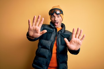 Young handsome skier man skiing wearing snow sportswear using ski goggles doing stop gesture with hands palms, angry and frustration expression