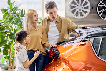 young adorable caucasian family with child in cars showroom, parents and son opted for the most convenient car