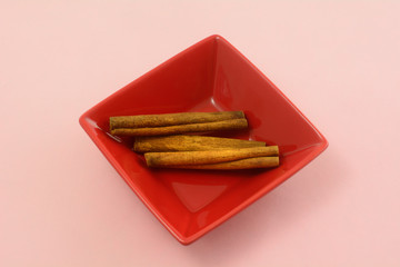 Cinnamon sticks spice in red square bowl on pink background