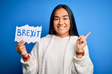 Canvas Print - Young asian woman holding paper with brexit message over isolated blue background very happy pointing with hand and finger to the side