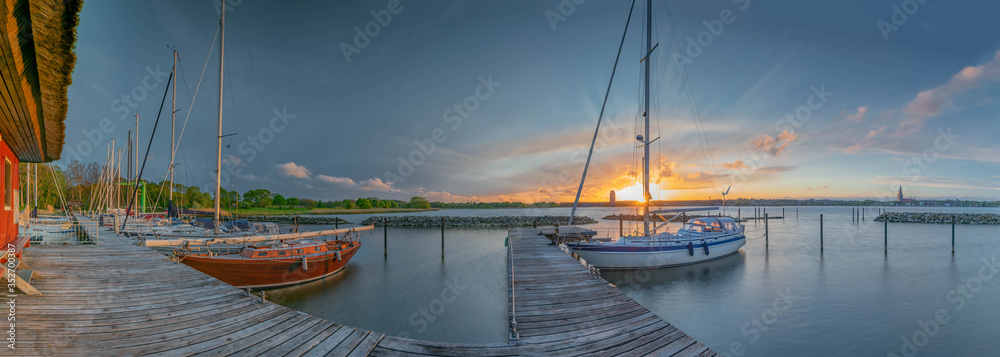 Sailing boats stowed at the pier, lit by the evening sun, sunset over small harbor with sailing boats, Schlei, Schleswig, Schleswig-Holstein, Germany - obrazy, fototapety, plakaty 