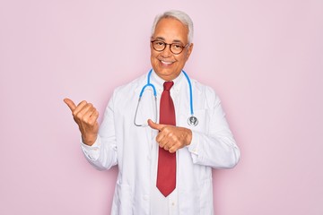 Canvas Print - Middle age senior grey-haired doctor man wearing stethoscope and professional medical coat Pointing to the back behind with hand and thumbs up, smiling confident