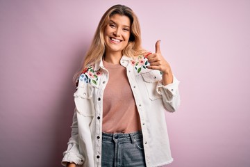 Sticker - Young beautiful blonde woman wearing casual jacket standing over isolated pink background doing happy thumbs up gesture with hand. Approving expression looking at the camera showing success.