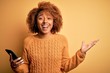 Young African American afro woman with curly hair having conversation using smartphone very happy and excited, winner expression celebrating victory screaming with big smile and raised hands
