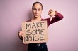 © Krakenimages.com - Beautiful activist woman holding banner with make some noise message over pink background with angry face, negative sign showing dislike with thumbs down, rejection concept