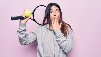 Sticker - Young beautiful sportswoman playing tennis using racket and ball over pink background covering mouth with hand, shocked and afraid for mistake. Surprised expression