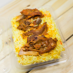 A plastic pack of lamb mandy rice on wood background. The best arabic food. Selective focus.