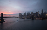 Fototapeta  - New York City, USA - 26 Dec 2019: Dramatic, colorful Sunset at the East River with Manhattan Skyline Lights and Brooklyn Bridge