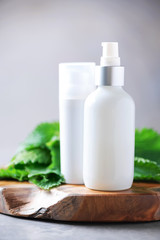 Wall Mural - Nettle lotion, cream, shampoo or soap in white bottle and fresh nettles leaves on grey background. Medicinal herb for health and beauty, skin care and hair treatment.