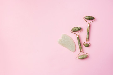 Green jade face roller and gua-sha scraper for facial acupuncture massage on pink background. Copy space. Skin care, face treatment