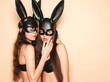 Leinwandbild Motiv Two sexy beautiful women wearing carnival black mask of Easter bunny rabbit.Hot brunette girls posing near wall in studio. Seductive models in nice lingerie