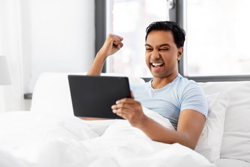 Sticker - people, bedtime and rest concept - happy smiling indian man with tablet pc computer lying in bed and making winning gesture at home