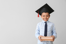 Little African-American Boy In Graduation Hat And With Books On Grey Background