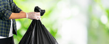 Close Up Man Hand Hold Black Trash Bag To Go To Throw In The Bin Isolated (clipping Path) On Blurred Green Outdoor Park Background With Copy Space For World Entertainment Day And Save Ecology Concept