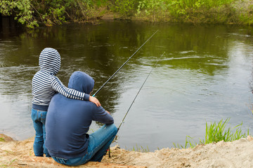 Back view of father and son fishing together, father teaching little young son to be a fisherman near the river. Concept of father's day.