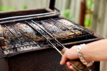 Wall Mural - Men grilling fish mackerel on barbecue cooked on the grill in the open air flow, tasty and fresh food, picnic, party, outdoor recreation. Barbeque in the garden in summer at home. .