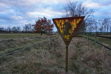 Triangular Railway Sign, Very Old And Rusty. Abandoned Railroad Overgrown With Grass