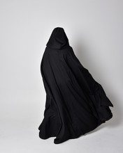 Fantasy Portrait Of A Woman Wearing Long Black Cloak. Full Length Standing Pose  With Back To The Camera, Isolated Against A Studio Background.