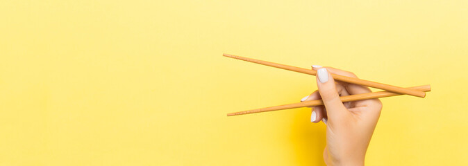 Wooden chopsticks holded with female hands on yellow background. Ready for eating concepts with empty space