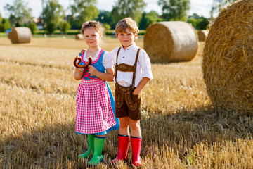 Wall Mural - Two kids in traditional Bavarian costumes in wheat field. German children eating bread and pretzel during Oktoberfest. Boy and girl play at hay bales during summer harvest time in Germany.