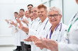 © ASDF - smiling female doctor standing in front of her applauding colleagues.