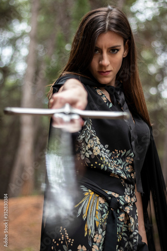 Fotografía Woman in the forest dressed in a tunic holding a large sword