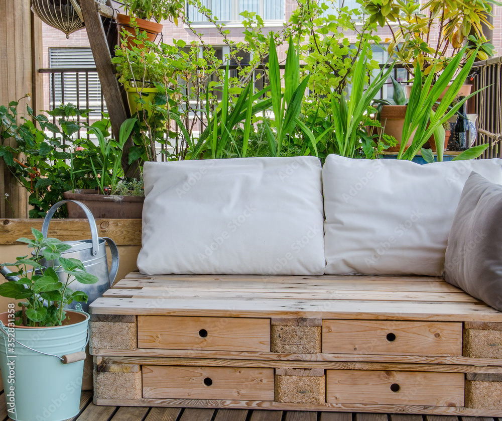 Wooden pallet couch on balcony with plants in background - obrazy, fototapety, plakaty 