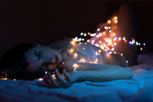 Beautiful Thin Girl In A Bra And Panties Lying On Her Bed With The Room Illuminated Only By Small Light Bulbs