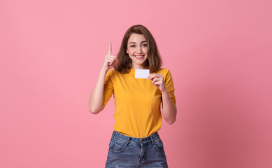 Wall Mural - Young smiling beautiful woman in yellow shirt showing credit card in hand over pink background.