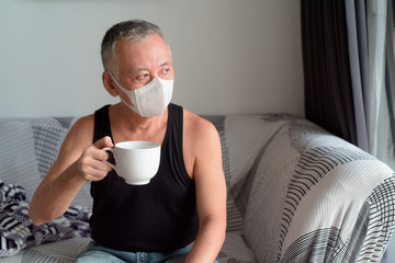 Poster - Mature Japanese man with mask thinking and drinking coffee at home under quarantine