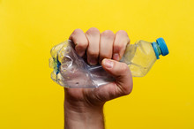 Crumpled Plastic Bottle In A Man's Hand Of Water On A Yellow Background. Ecology Environment Protection. Stop Plastic Concept. Save Nature.