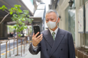 Poster - Mature Japanese businessman with mask using phone in the city