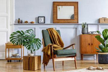 Stylish interior of living room with design armchair, vintage commode, mirror, shelf, tropical leaves, coffee table, plants, decoration, carpet and persnoal accessories in home decor.