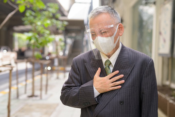 Sticker - Stressed mature Japanese businessman with mask and face shield getting sick in the city