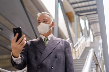 Poster - Mature Japanese businessman with mask using phone while going down the stairs in the city