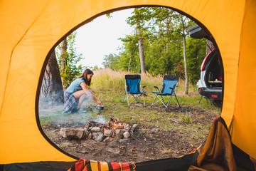 Wall Mural - view from camping tent woman cooking on burner near bonfire