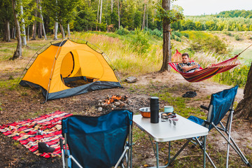 Wall Mural - man laying on hammock at lake beach near camp fire