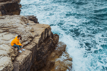 Wall Mural - woman siting on the edge of the cliff looking on big waves