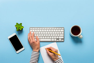 Woman works in the office on a blue background.Only hands Concept workspace, working at a computer, freelance, design. phone, flower, pencil. Banner. Flat lay, top view