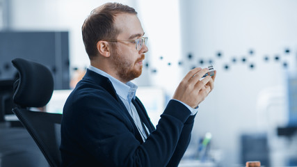 Aufkleber - Electronics Factory: Male Electrical Engineer Holds PCB Prototype, Works on Personal Computer. Modern High-Tech Industrial Factory Office.