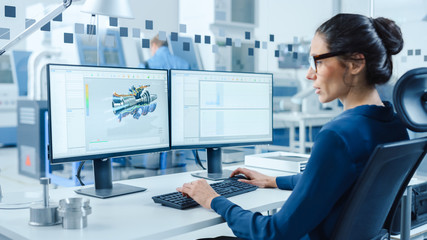 Poster - Industrial Female Engineer Working on a Personal Computer, Two Monitor Screens Show CAD Software with 3D Prototype of Engine and Charts. Modern Factory with High-Tech Machinery