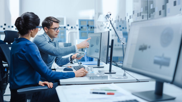 Modern Factory: Male Industrial Engineer Explains to Female Project Supervisor Functions of the Machine Part Comparing it to one on Computer Screen. They use CAD Software for Design, Development