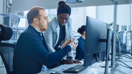 modern factory: female project supervisor talks to a male industrial engineer who works on computer.