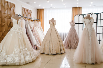 Beautiful wedding dresses, bridal dress hanging on hangers and mannequin in studio. Fashion look. Interior of bridal salon.